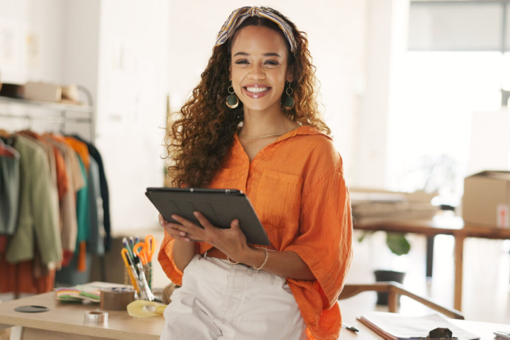 Empreendedora sorrindo ao telefone enquanto trabalha no notebook em seu ateliê de moda